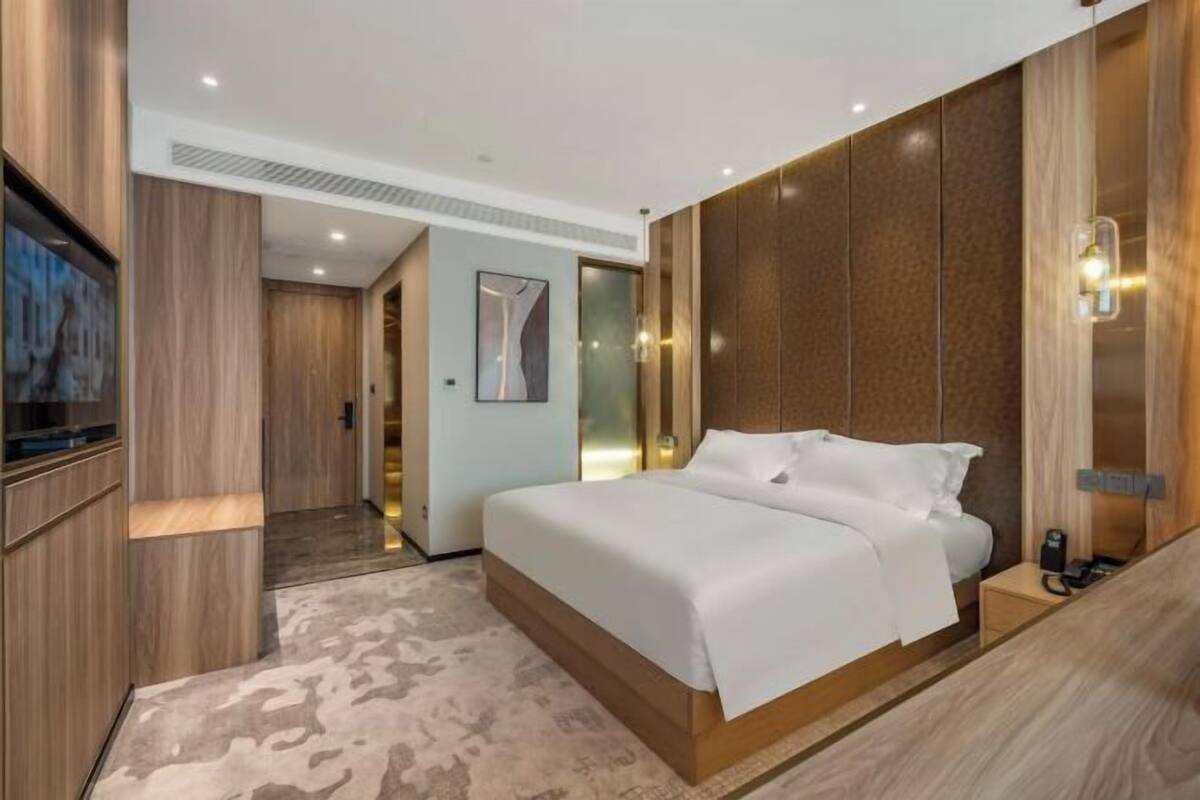 Een moderne hotelkamer met een groot bed, houten lambrisering, een flatscreen televisie en een klein nachtkastje.