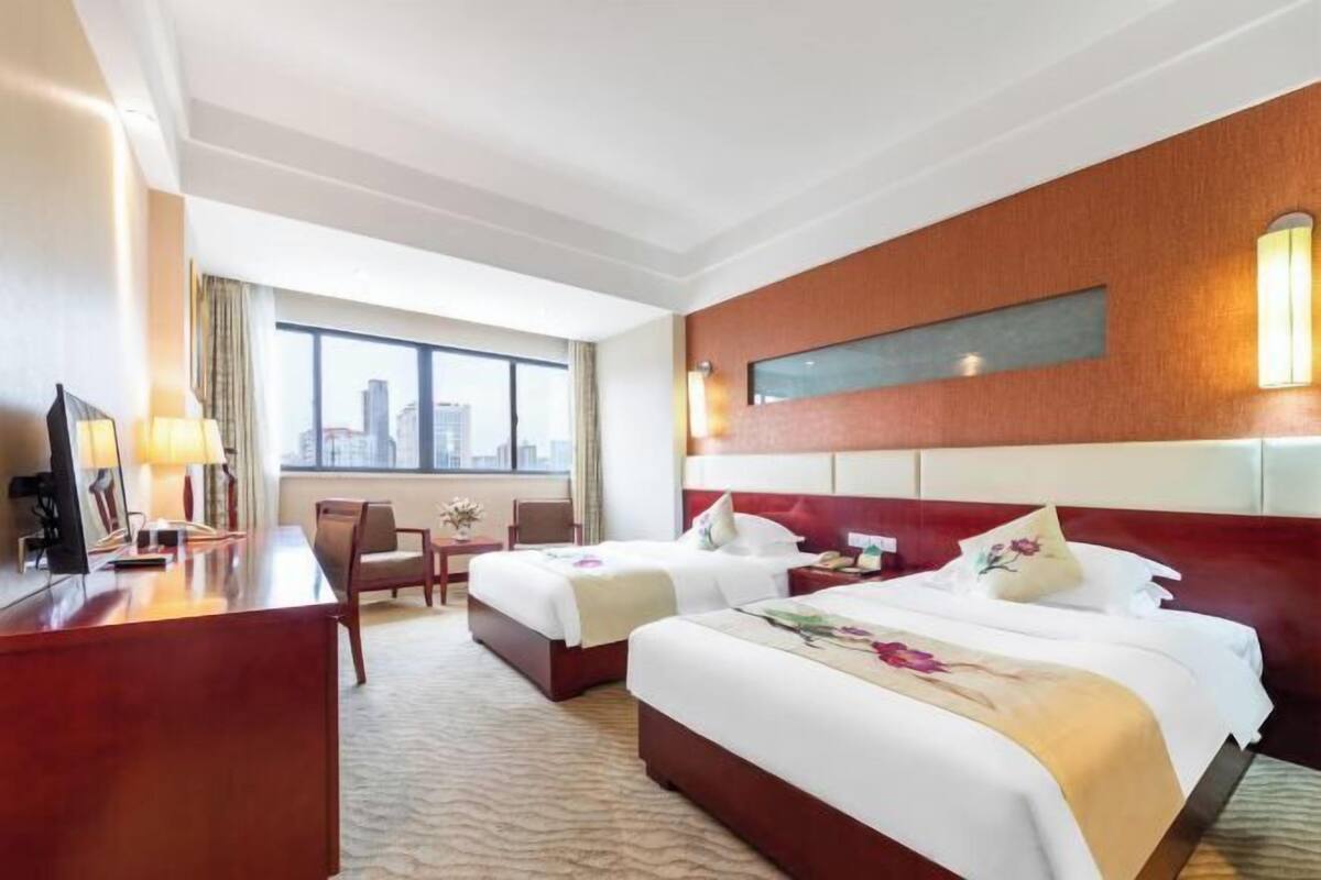 Hotelkamer met twee bedden, een bureau, een stoel en een groot raam met uitzicht op de stad.