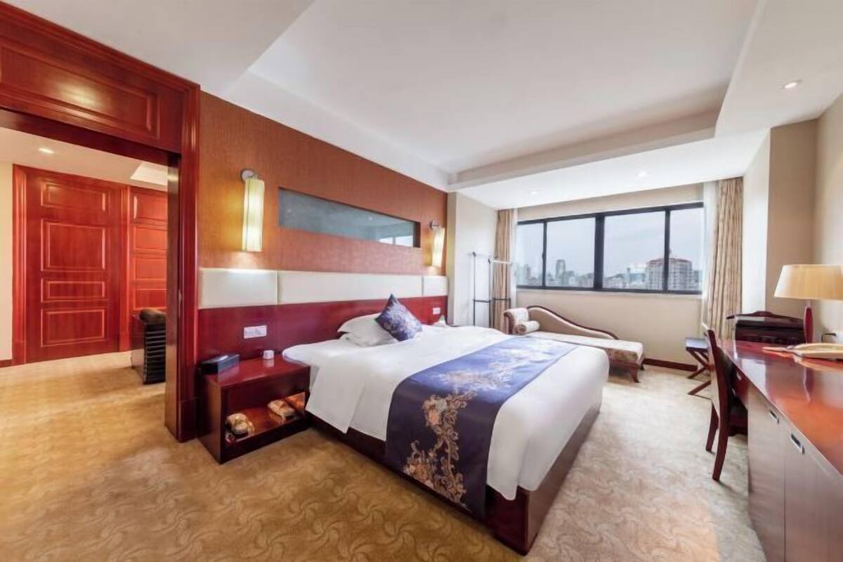 Een hotelkamer met een groot bed, een bureau, een stoel en uitzicht op de stad.