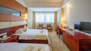 Een hotelkamer met twee bedden, een bureau, een televisie en een raam met gordijnen.