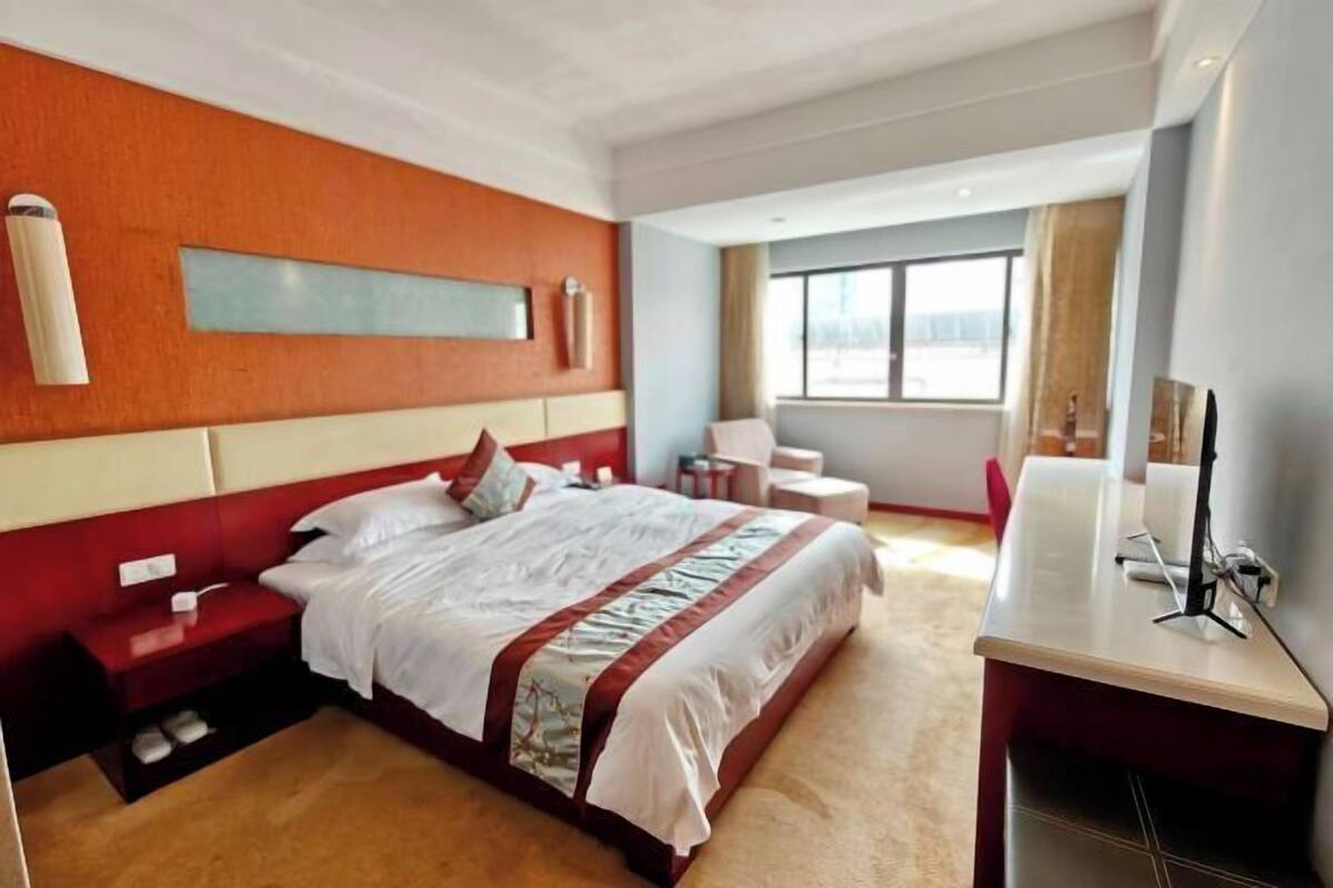 Een hotelkamer met een groot bed, een bureau, een stoel, een raam en een wandlamp.