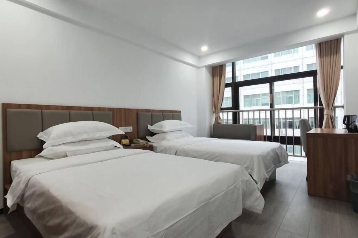 Een hotelkamer met twee bedden, een bureau en een groot raam met gordijnen.