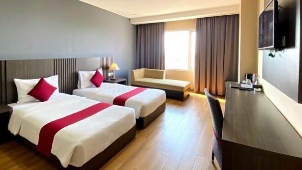 A hotel room with two beds, a desk, a chair, a TV, and a window with curtains. - Merapi Merbabu Hotels Bekasi (Rawalumbu)