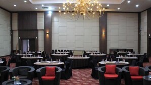 A conference room with round tables, black chairs with red cushions, and a chandelier. - Merapi Merbabu Hotels Bekasi (Rawalumbu)