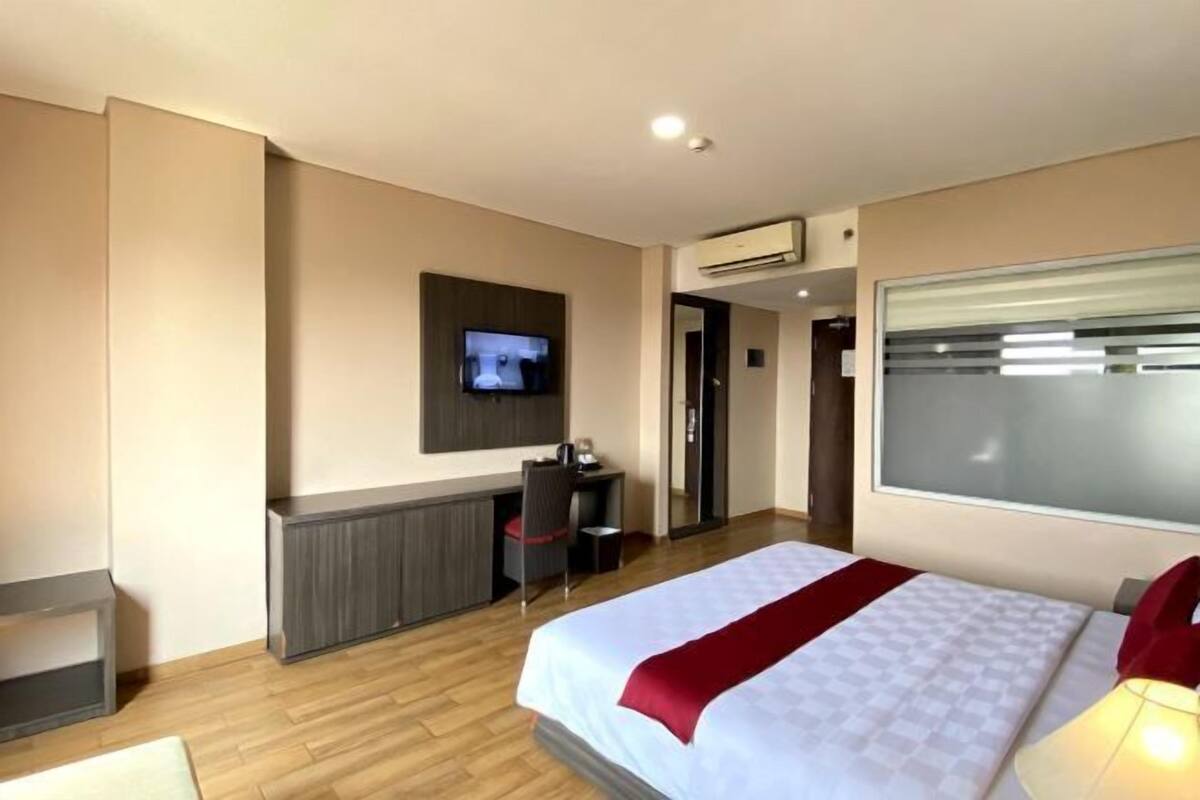 A hotel room with a bed, a desk, a TV, and an air conditioning unit.