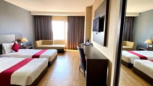 A hotel room with three beds, a desk, a TV, and a large window with curtains. - Merapi Merbabu Hotels Bekasi (Rawalumbu)
