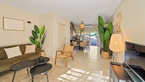 A modern living room with a sofa, two small tables, a chair, a TV, and large plants.