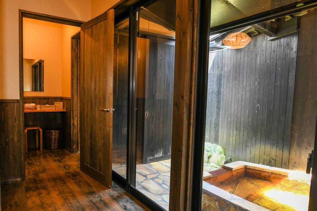 A wooden interior hallway leading to a stone-floored outdoor area with a wooden fence and a stone bench.