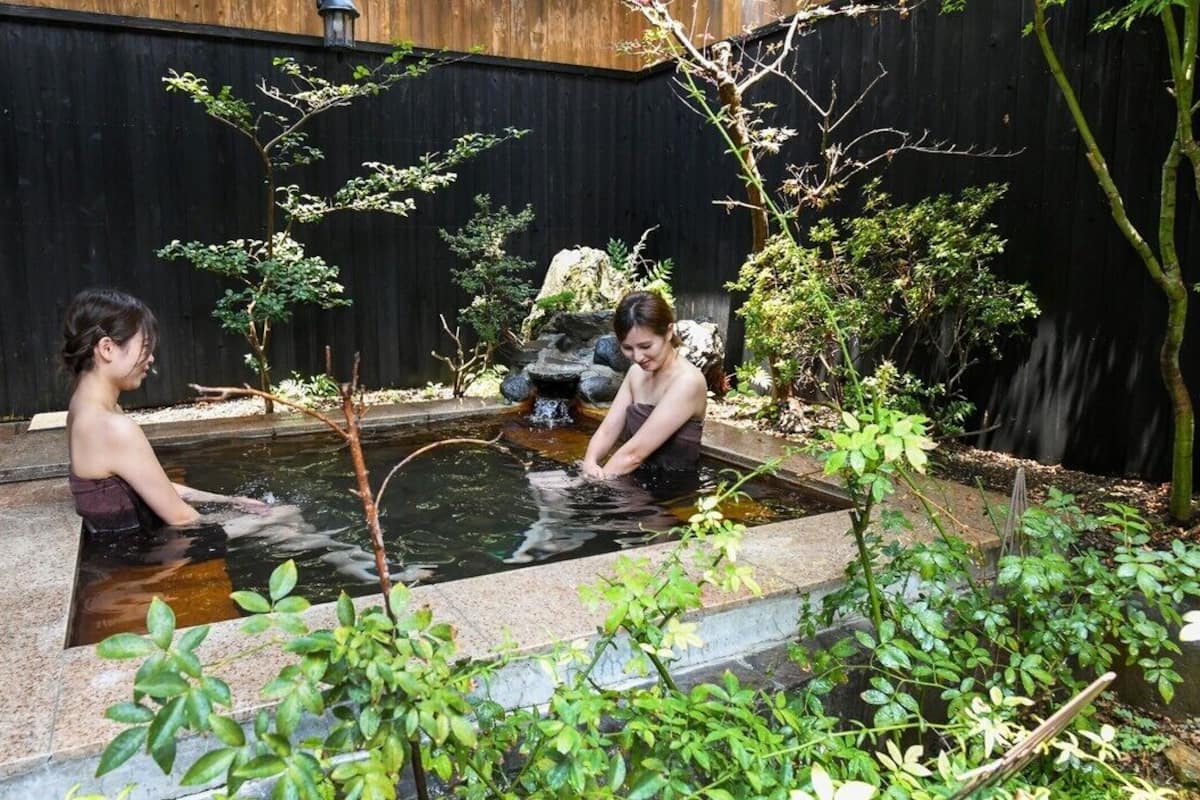 En lille udendørs pool med to personer, omgivet af grøn vegetation og et træhegn.