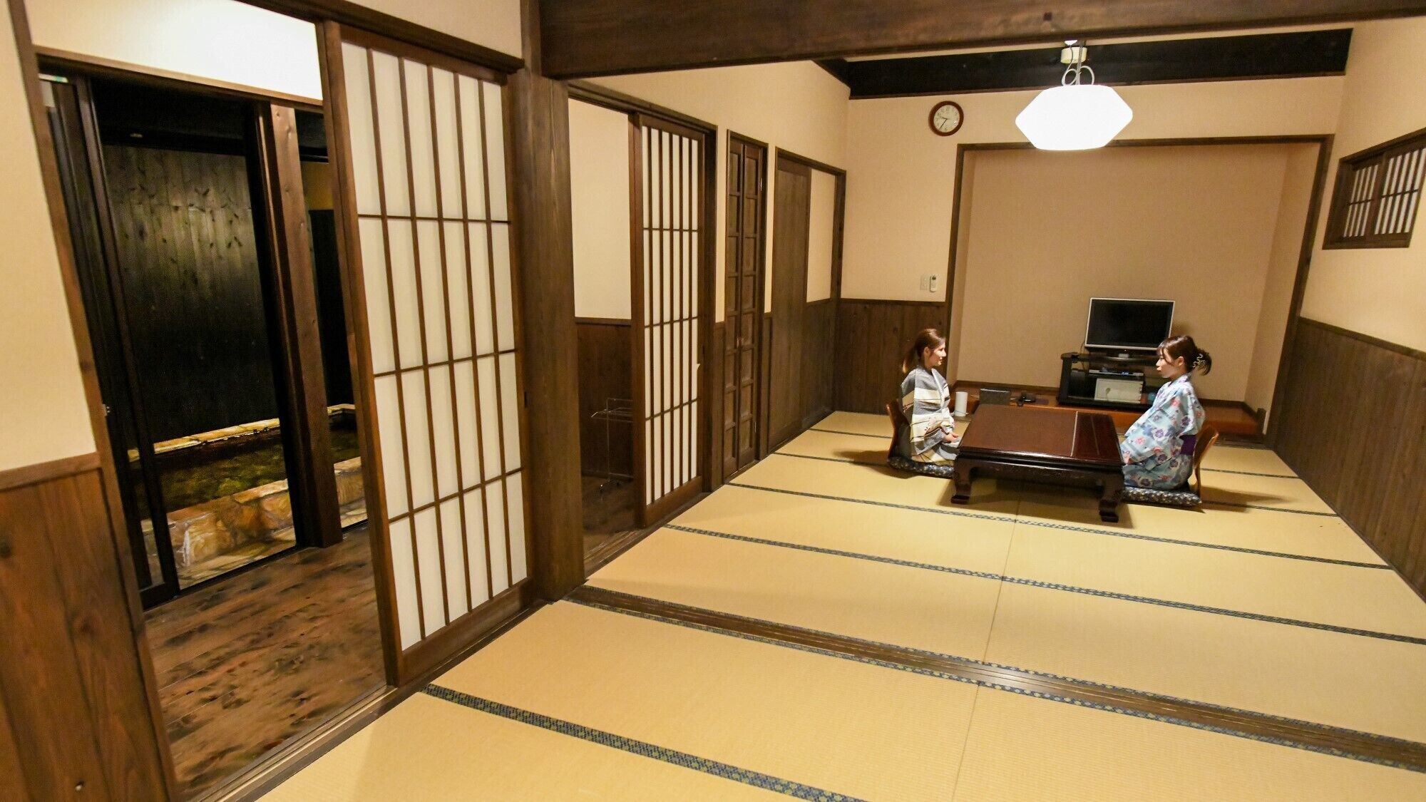 A traditional tatami mat room with sliding doors, a television, and a clock on the wall.