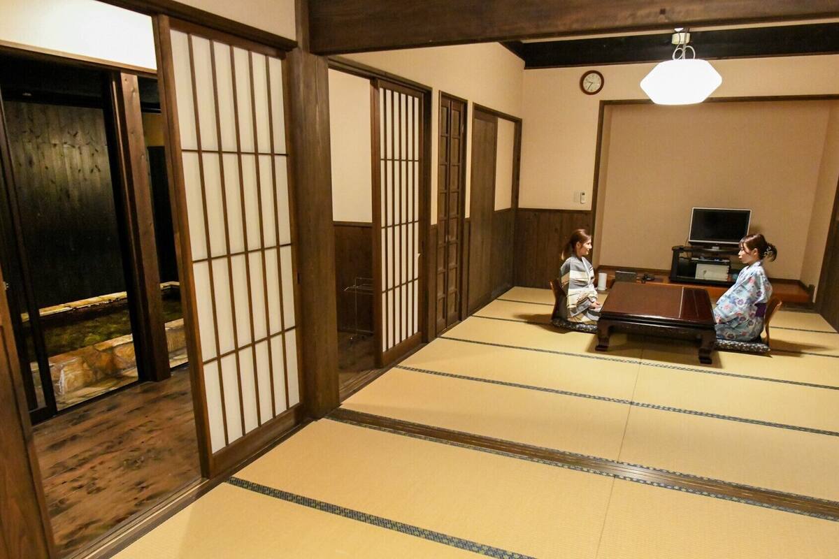 A traditional tatami mat room with sliding doors, a television, and a clock on the wall.
