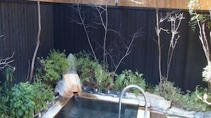 Ein rechteckiges Whirlpool mit Steinverkleidung, einer Holzdielen-Terrasse und einem dunklen Zaun im Hintergrund.