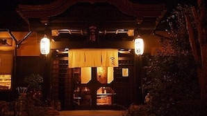 Ein traditionelles japanisches Gebäude bei Nacht mit Holzeingang, Laternen und einem überdachten Bereich mit Stufen.