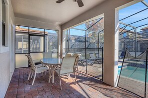 Relax in this serene patio area with a table and wicker chairs, surrounded by glass walls offering views of the neighborhood.