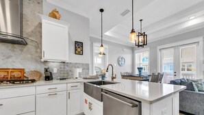 A modern kitchen with white cabinetry, stainless steel appliances, and pendant lighting.