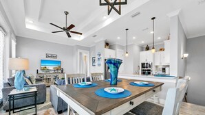 A spacious dining area with a wooden table, blue placemats, and a large vase centerpiece.