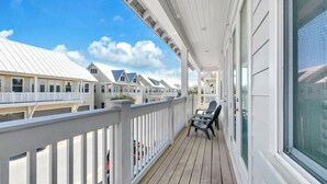 A covered balcony with a view of adjacent buildings, a wooden deck, and a seating area with chairs.
