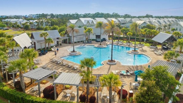 A resort with a central pool surrounded by lounge areas and palm trees.