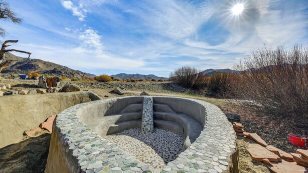A circular stone structure with a central water feature, surrounded by a natural landscape with mountains in the background. - Mtn-View Weldon Home: Walk to Pacific Crest Trail (Weldon)