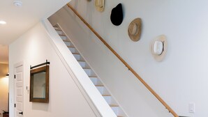 A staircase with white railings and wooden steps, leading to a landing with a mirror and wall-mounted hats. - Modern Cowboy Retreat Near Downtown Lockhart (Lockhart)