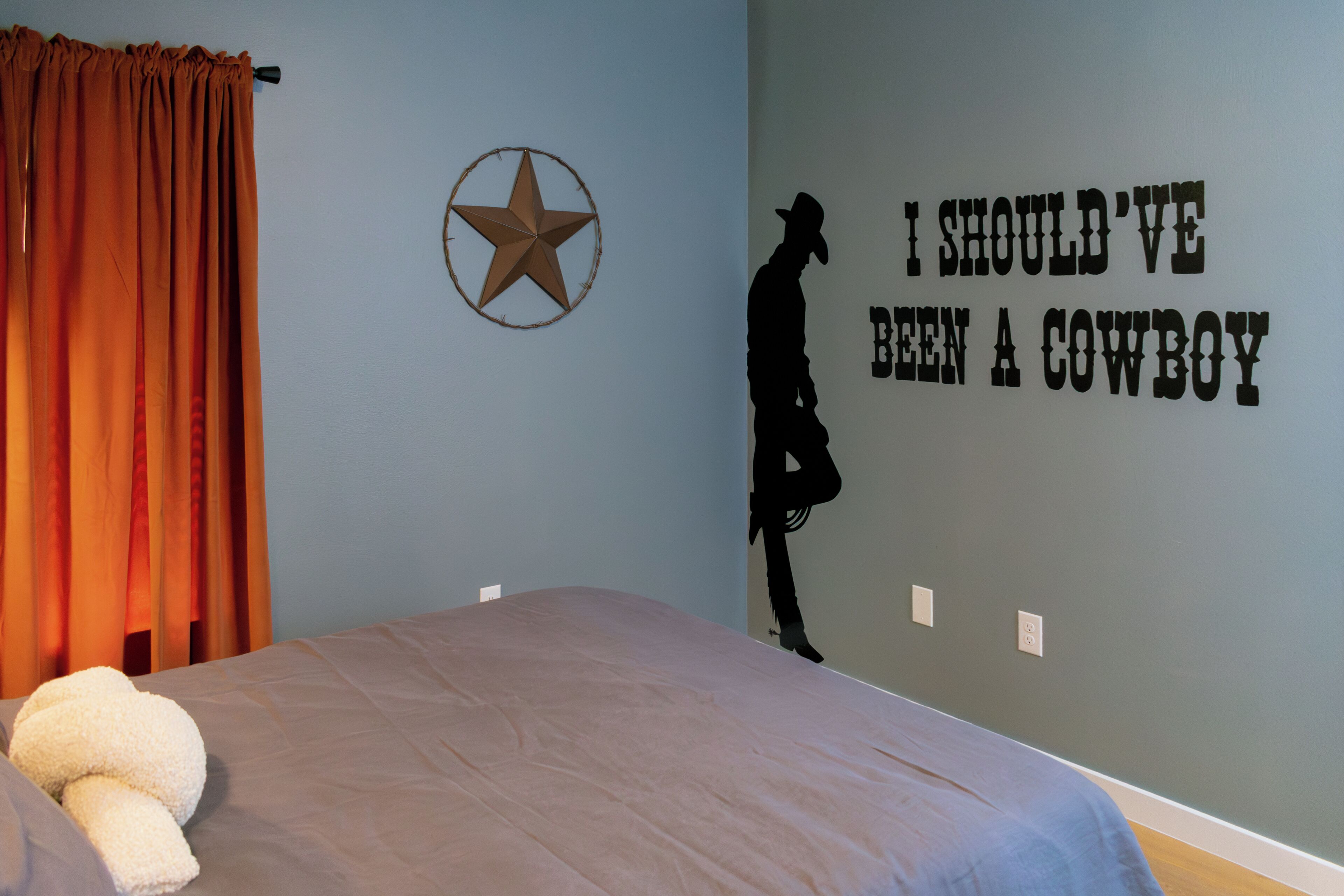 A bedroom with a bed, a wall decoration of a cowboy silhouette, and a star on the wall.