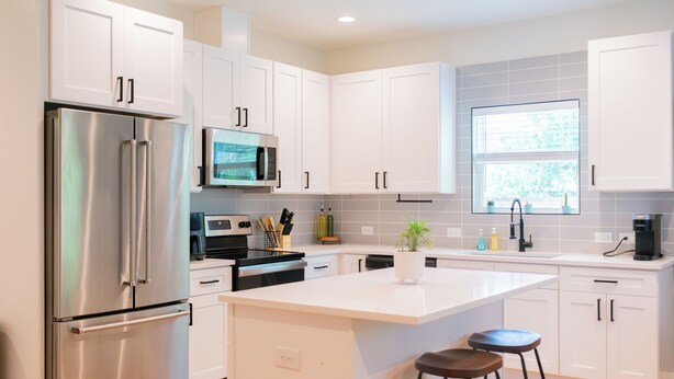 A modern kitchen with white cabinets, stainless steel appliances, and a central island with stools. - Modern Cowboy Retreat Near Downtown Lockhart (Lockhart)