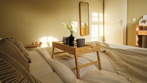 Ein ordentlich bezogenes Bett mit einem Tablett, das zwei Tassen und einen Blumentopf enthält, ein Nachttisch mit einer Lampe und ein Spiegel an der Wand.