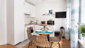 Una cucina compatta con mobili bianchi, un forno a microonde e un piccolo spazio pranzo con sedie in vimini e un tavolo apparecchiato per due persone.