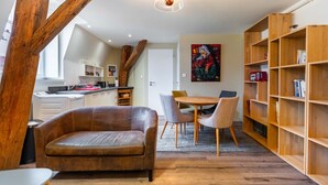 A modern living space with a leather sofa, dining table, chairs, and a wooden bookshelf.