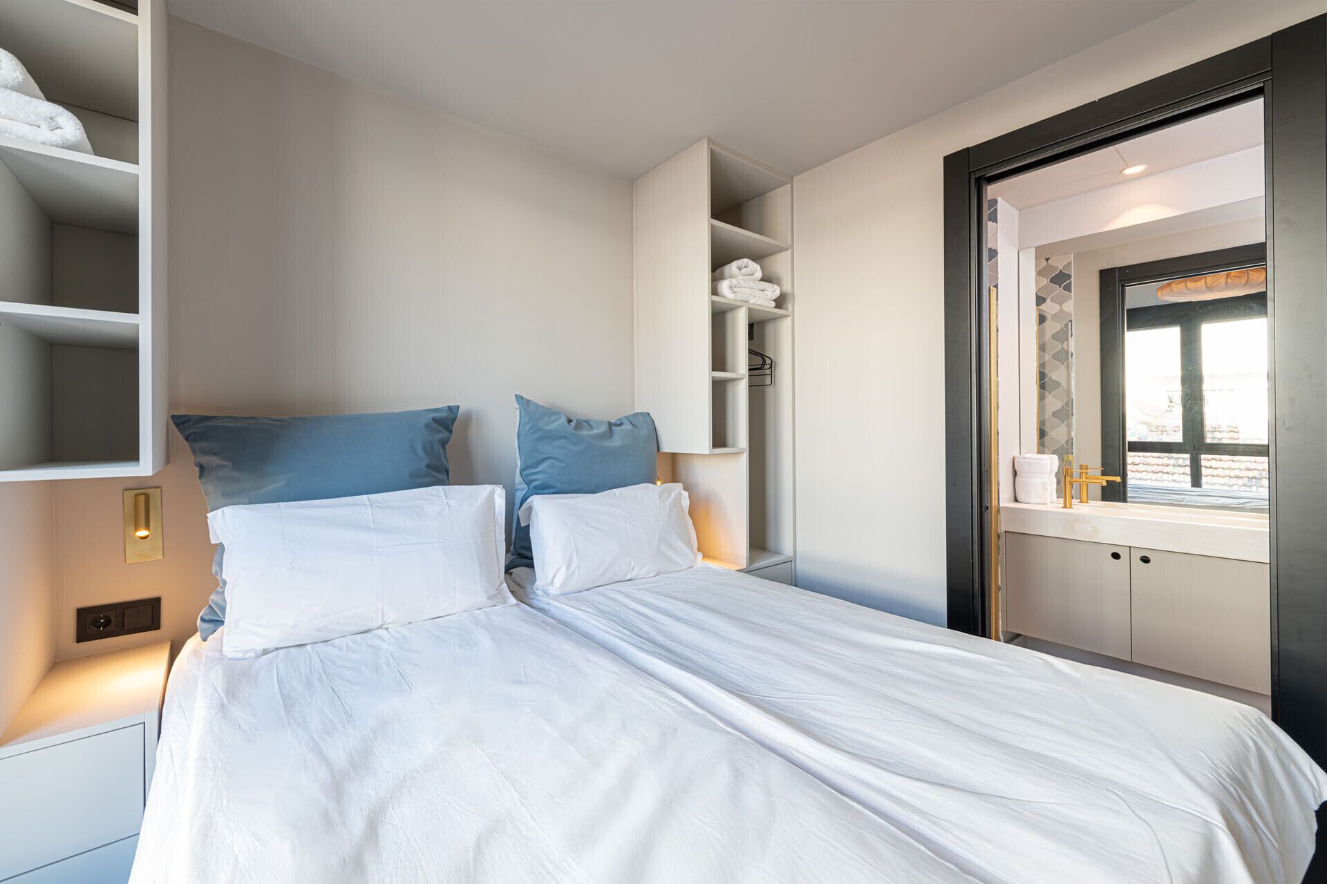 Quarto moderno com cama, duas almofadas, mesa de cabeceira, armário embutido e janela com vista.