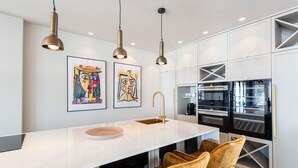 Una cocina moderna con encimera blanca, sillas doradas y electrodomésticos de acero inoxidable.