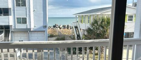 A balcony with a view of the beach, a building with a number '1610' sign, and a clear sky.