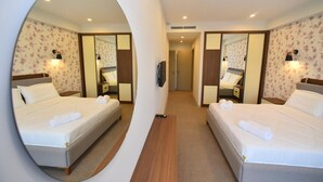 Una habitación de hotel con dos camas, un espejo, un televisor y un pasillo que conduce a otra habitación.