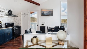 A modern kitchen with dark blue cabinets, a black stove, and a white backsplash. There is a dining area with a glass table, a globe, and a vase. A painting of mountains hangs on the wall. - 180 Degree view of the lake (Big Bear Lake)