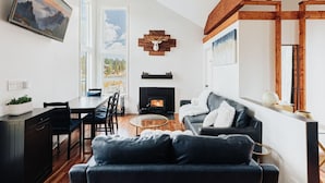 A modern living room with a fireplace, a black leather sofa, a dining area with a table and chairs, and a large window offering a view of the outdoors. - 180 Degree view of the lake (Big Bear Lake)