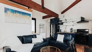 A modern living room with a dark leather sofa, a glass coffee table, and a kitchen area with a stove and cabinets. - 180 Degree view of the lake (Big Bear Lake)