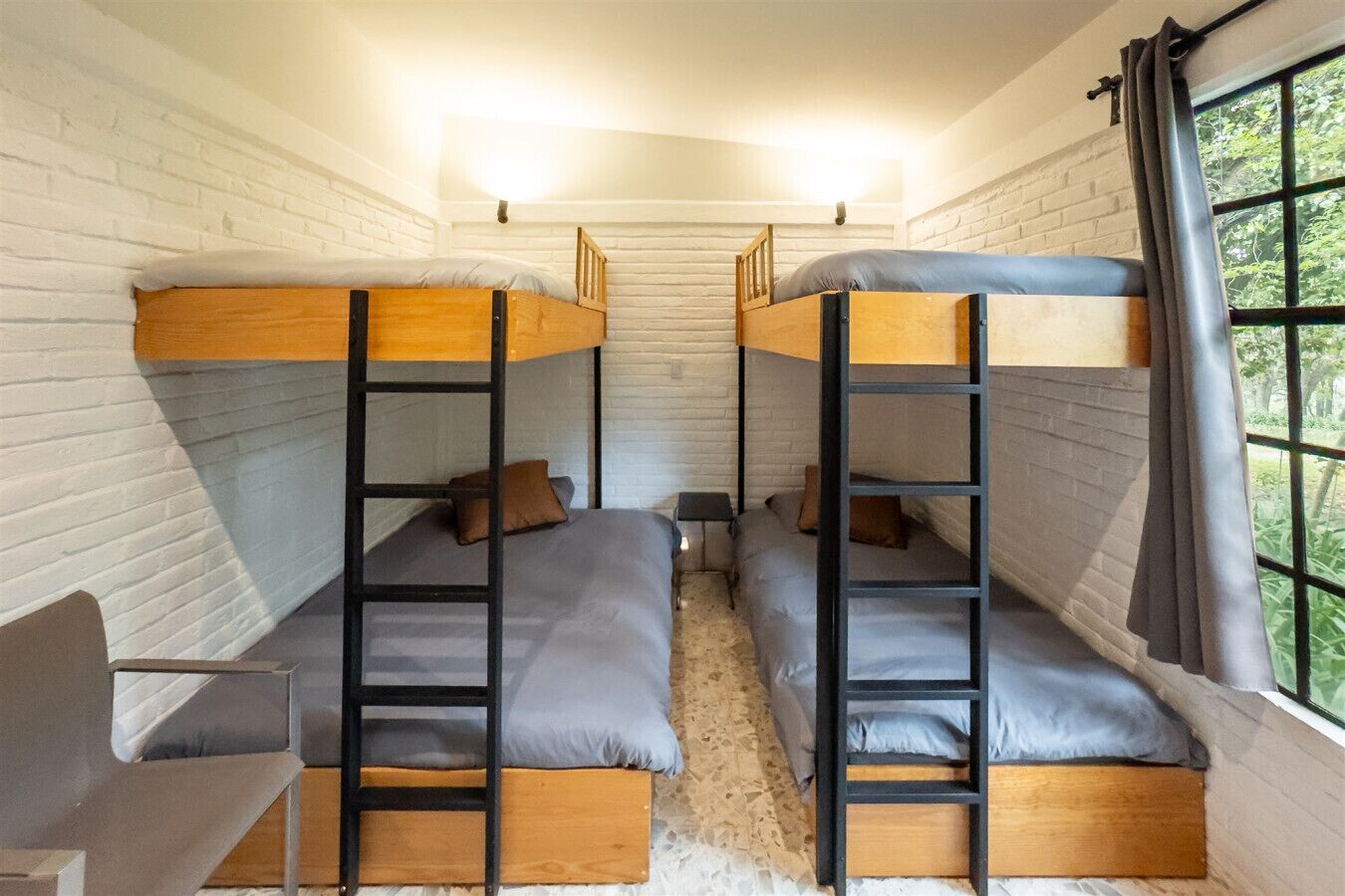 A room with three bunk beds, white brick walls, and a window with curtains.
