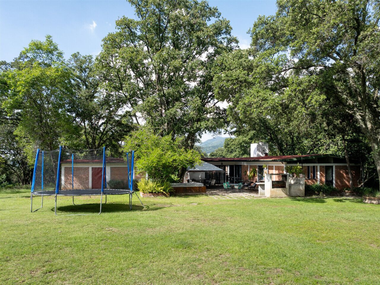 Un jardin avec un trampoline, un espace barbecue et une maison dotée d’une terrasse.
