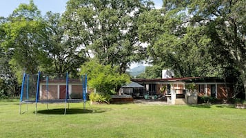 Un jardin avec un trampoline, un espace barbecue et une maison dotée d’une terrasse.