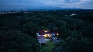 An aerial view of a house surrounded by dense forest, with a well-lit patio area and a visible garage. - Tepoztlán Escape with Jacuzzi, Fireplace & Games (San Miguel Cañadas)