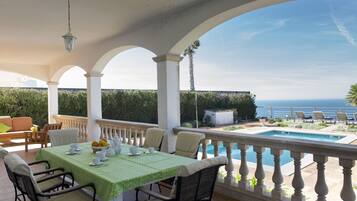 Un espacio al aire libre techado con piscina, asientos y vistas al mar.