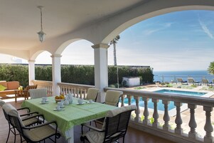 Un espacio al aire libre techado con piscina, asientos y vistas al mar.