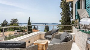 Ein Balkon mit Korbmöbeln, einem Grill und Blick auf das Meer.