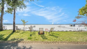 Terraza junto al lago con asientos exteriores y un hogar para fogata, con vista a un lago tranquilo y barcos amarrados.