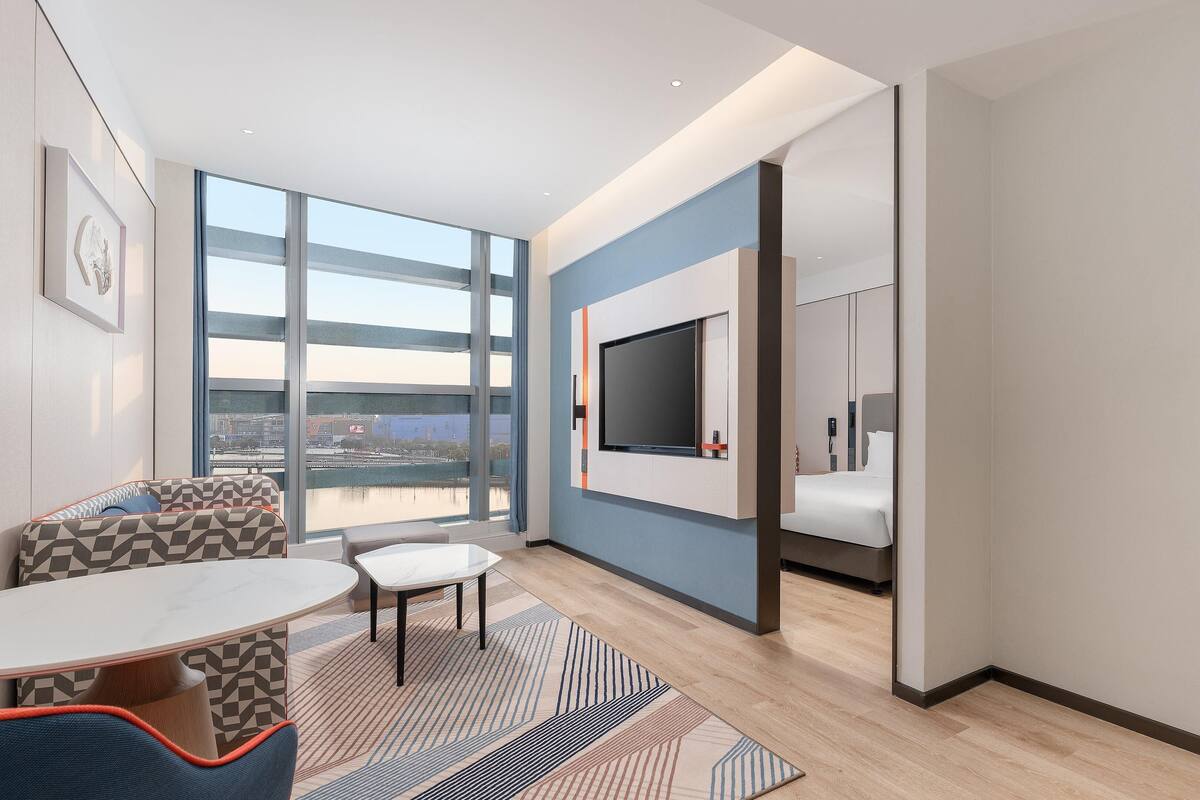 Une chambre d’hôtel moderne dotée d’une grande fenêtre, d’un téléviseur à écran plat, d’un lit et d’une salle de bain.