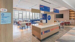 A modern cafe with a wooden reception desk labeled "EXPRESS COFFEE STATION," tables with chairs, and a large window providing natural light.