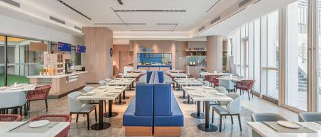 A modern restaurant with a central seating area, multiple tables, and a counter with a digital menu display.