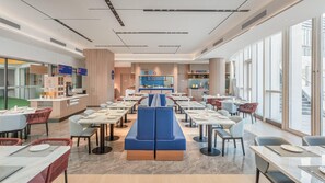 A modern restaurant with a central seating area, multiple tables, and a counter with a digital menu display.