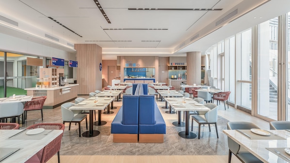 A modern restaurant with a central seating area, multiple tables, and a counter with a digital menu display.