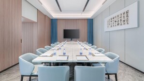 Un salón de conferencias con una larga mesa, sillas, una pantalla y una pared decorada con caligrafía.